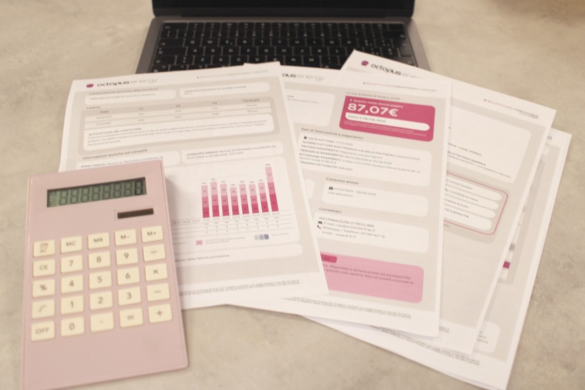 A close-up of an insurance quote worksheet beside a calculator, with rows of business exposures being used to build a final policy price, alongside a pile of application forms and a pen